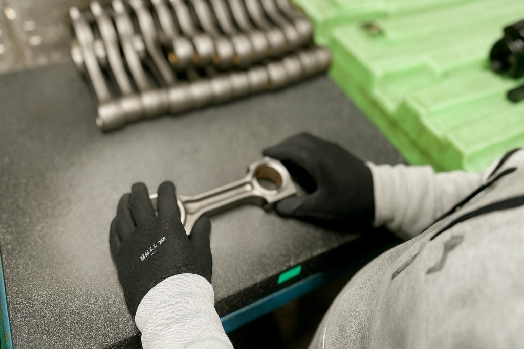 Worker inspecting a metal component on a black workbench, highlighting precision in inspection and sorting services for manufacturing quality assurance.
