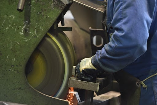 Worker operating a grinding machine in a manufacturing setting, sparks flying, emphasizing quality control and precision in industrial processes.